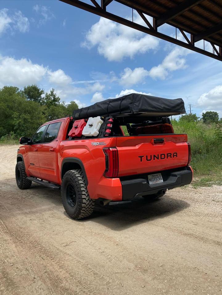 matte black rear bumper covers installed on a red 2022-2024 Toyota Tundra situated under a bridge, chrome delete adventure