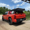 matte black rear bumper covers installed on a red 2022-2024 Toyota Tundra situated under a bridge, chrome delete adventure